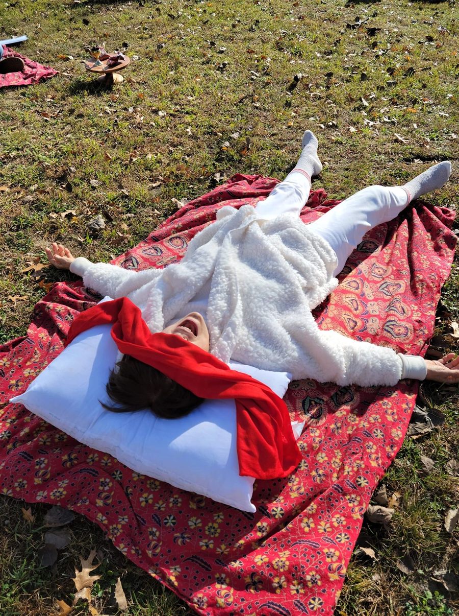 A participant in white lying joyfully on a red patterned blanket in the grass after ceremony
